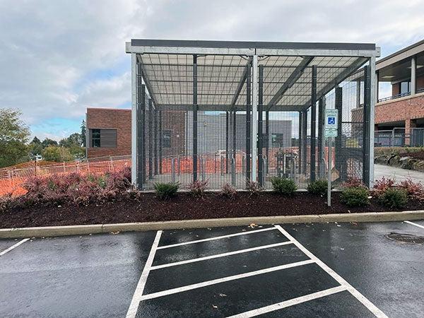 a fenced in space with bike racks inside and plants on outside